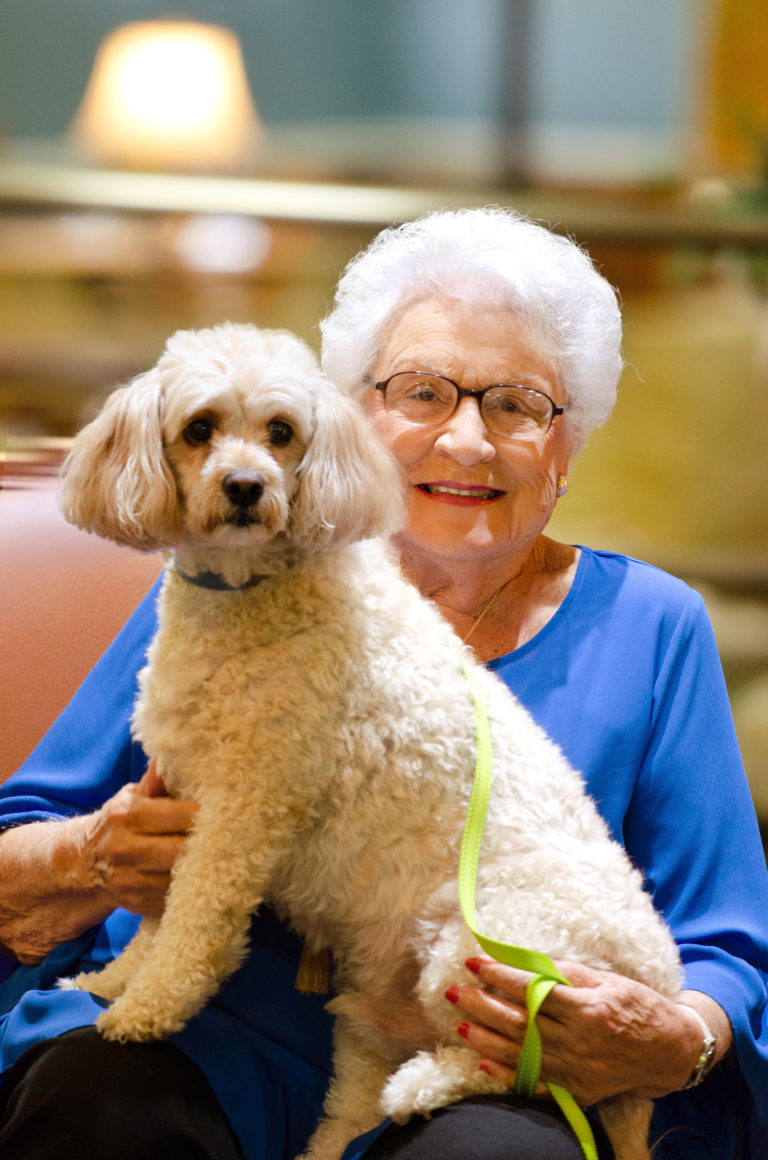 A resident in the common area smiling with her dog on her lap
