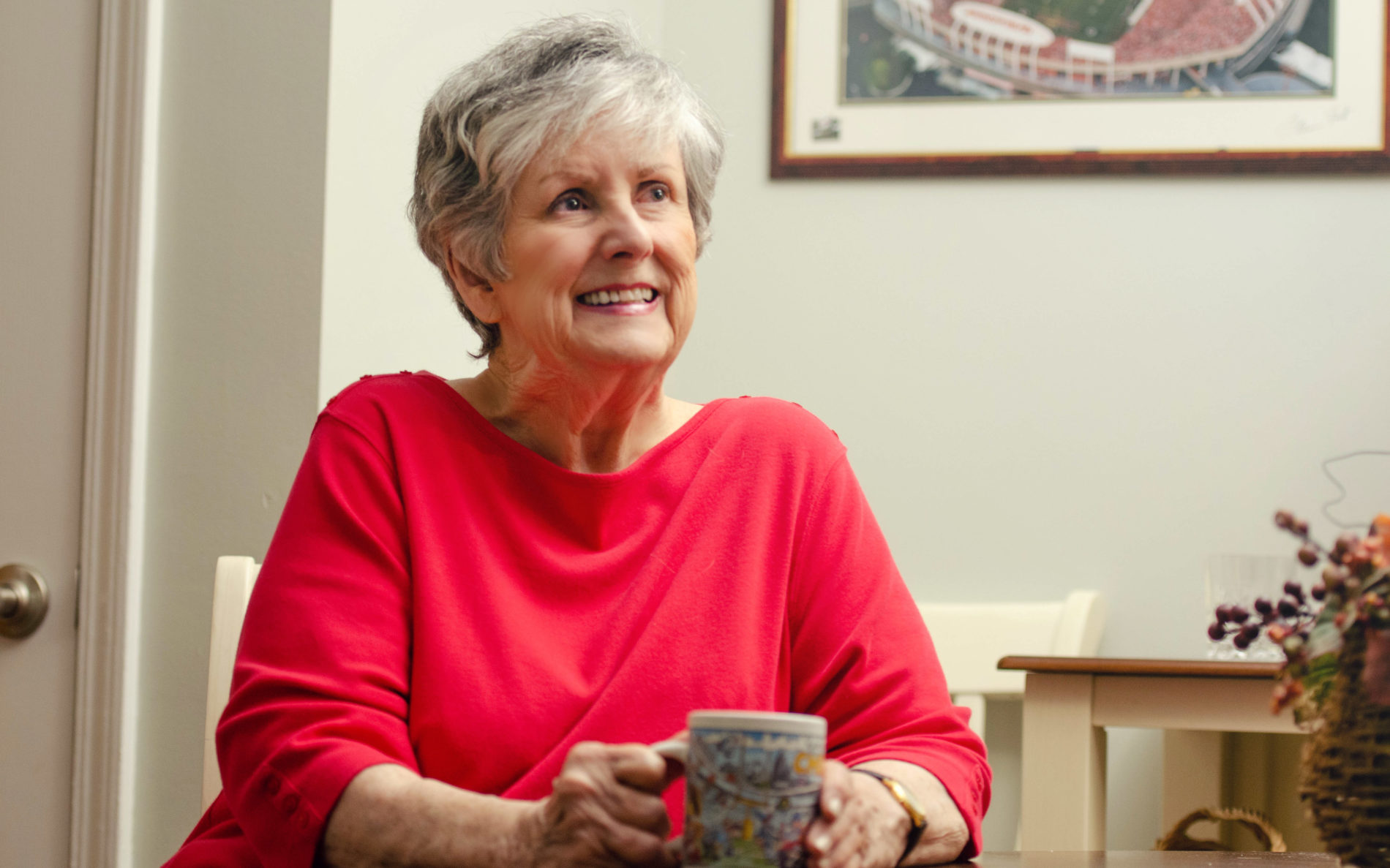 A woman resident in pink, enjoying a cup of coffee in her room as she smiles up at the camera