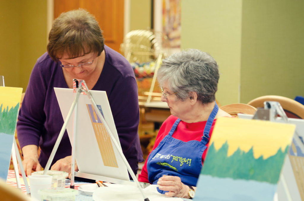 Two female residents painting on canvases during their activity.