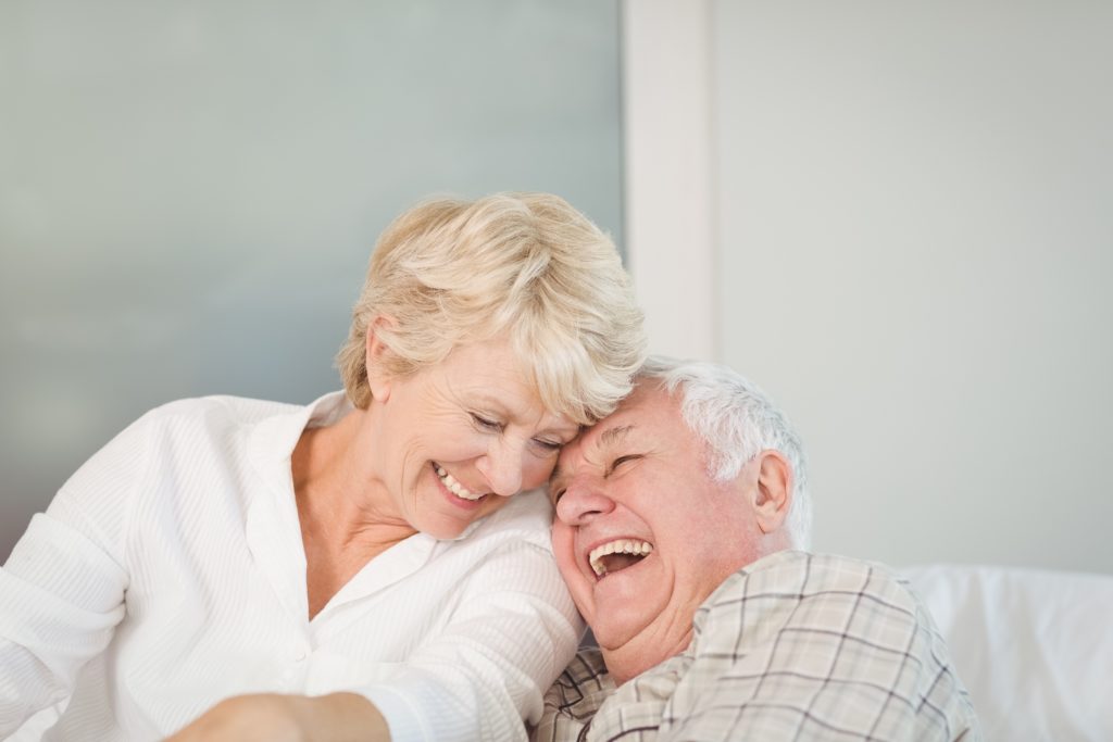 A senior couple laughing together with their heads pressed together, enjoying each other