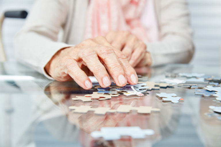 an elderly woman trying to piece together a puzzle on a table