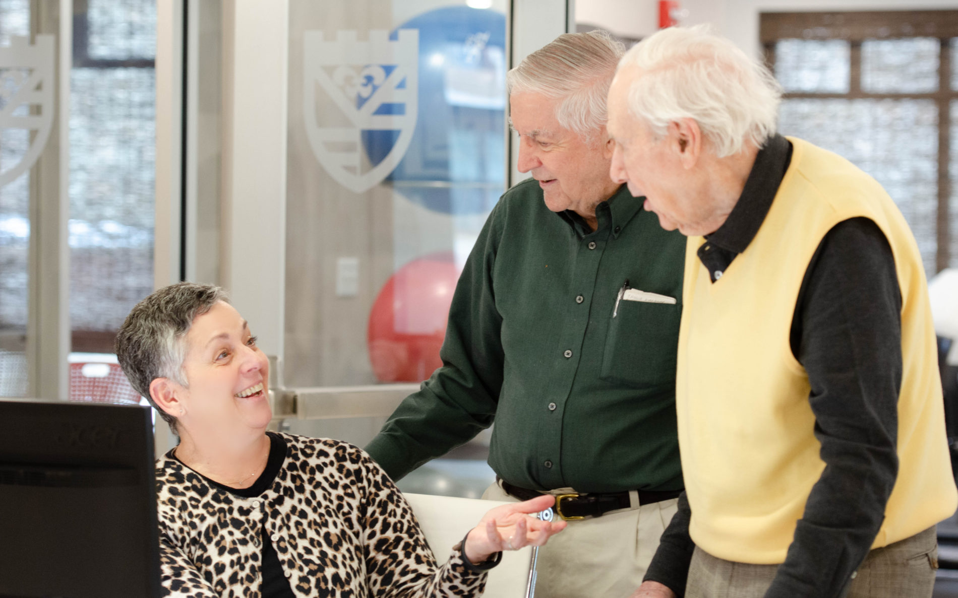Two residents visiting with the woman at the front desk, sharing conversation and smiling