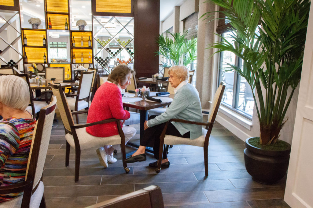 Two residents smiling and engaging in conversation in the dining area as their chairs face each other