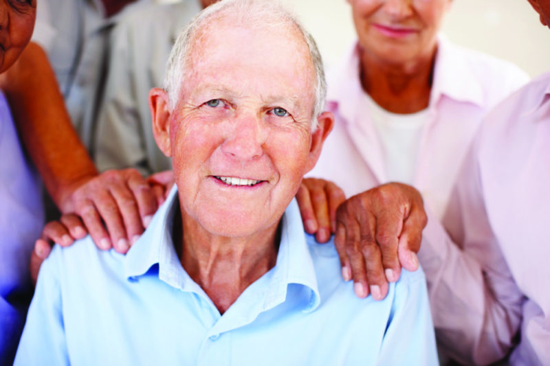 senior man smiling with hands on shoulders