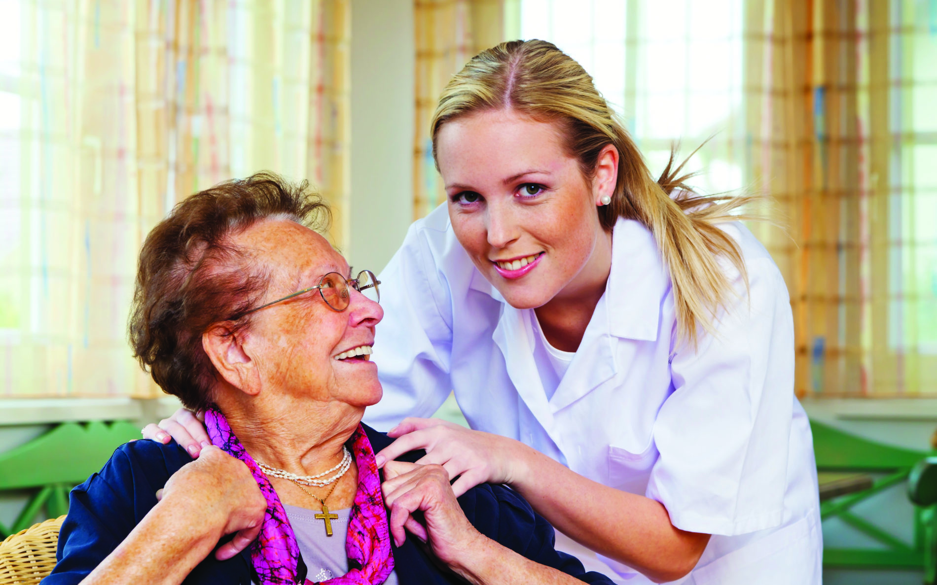 A woman resident smiling at her nurse, as her nurse looks and smiles at the camera.