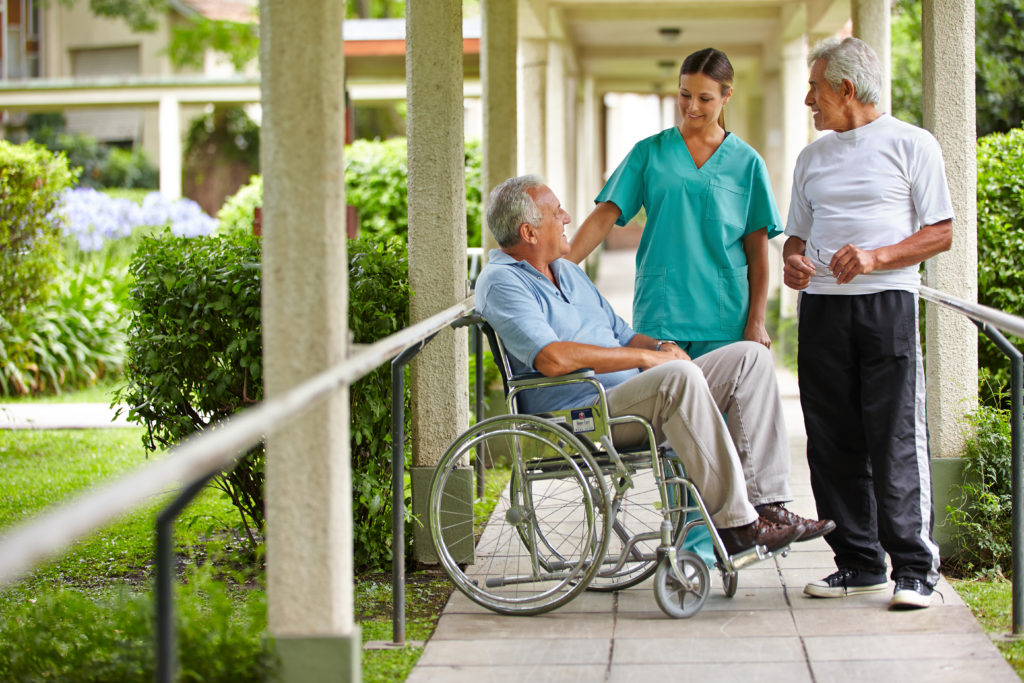 A resident in a wheelchair chatting with doctors as he looks up at them and smiles