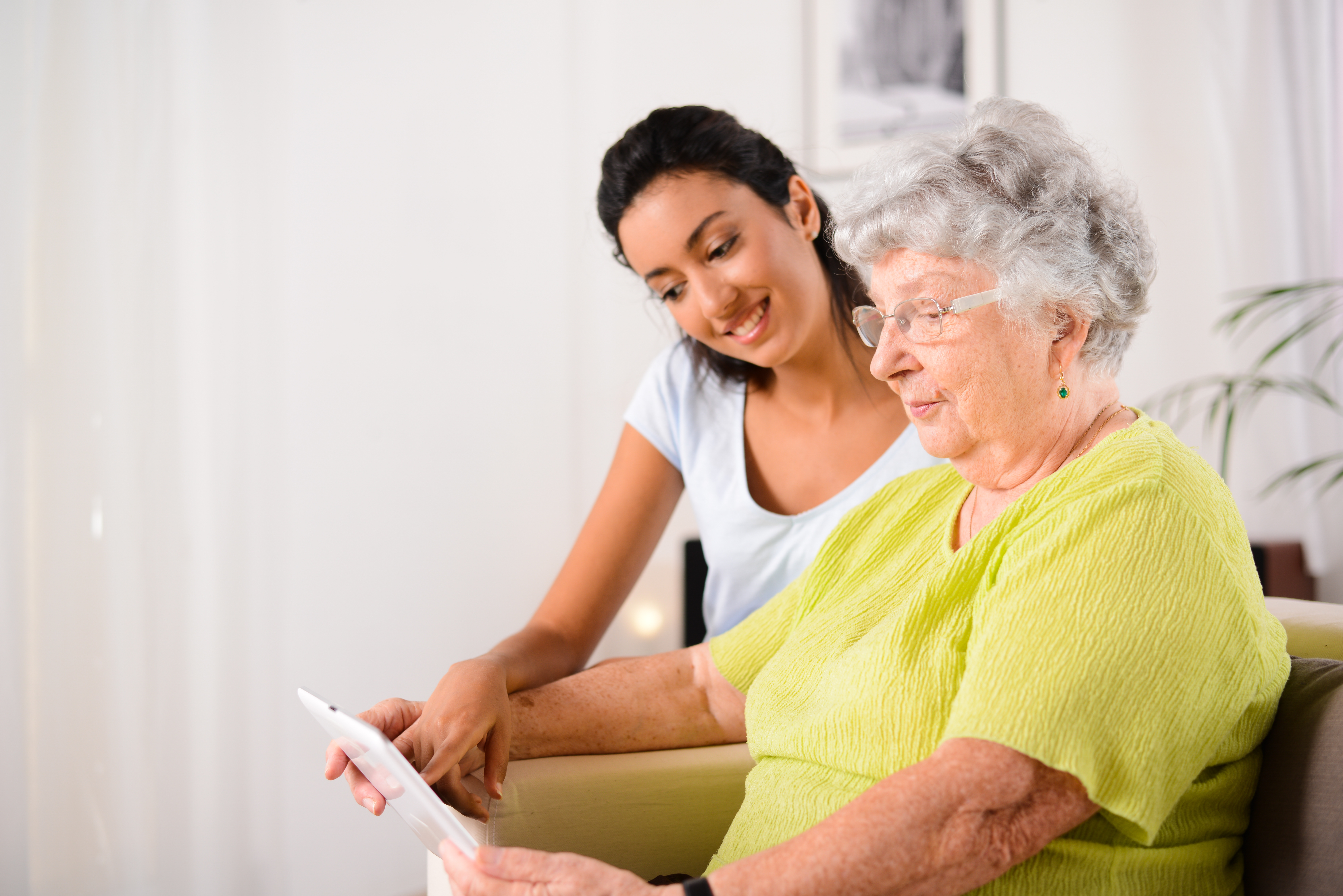 cheerful young girl with an elderly woman playing with digital tablet at home