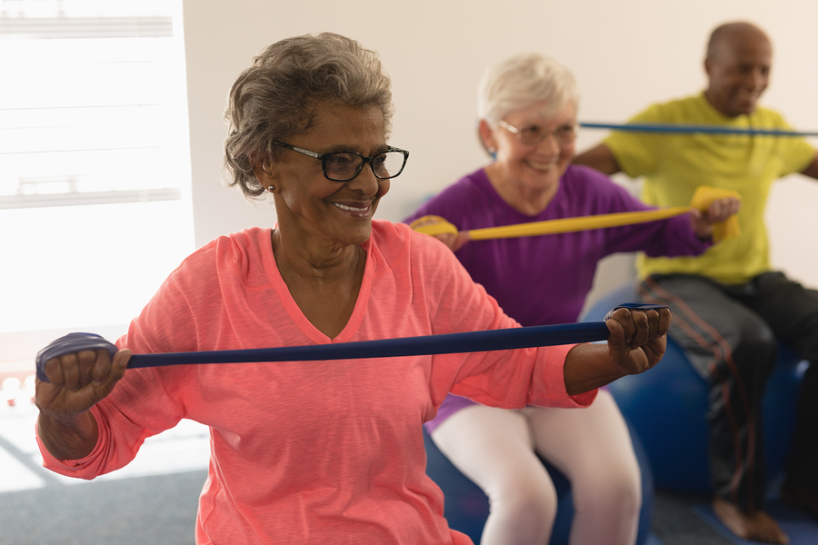 Happy senior woman exercising with resistance band in fitness studio