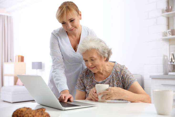 Senior woman and caregiver with laptop at home