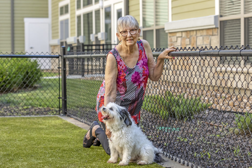 Elderly woman kneeling with dog near gate