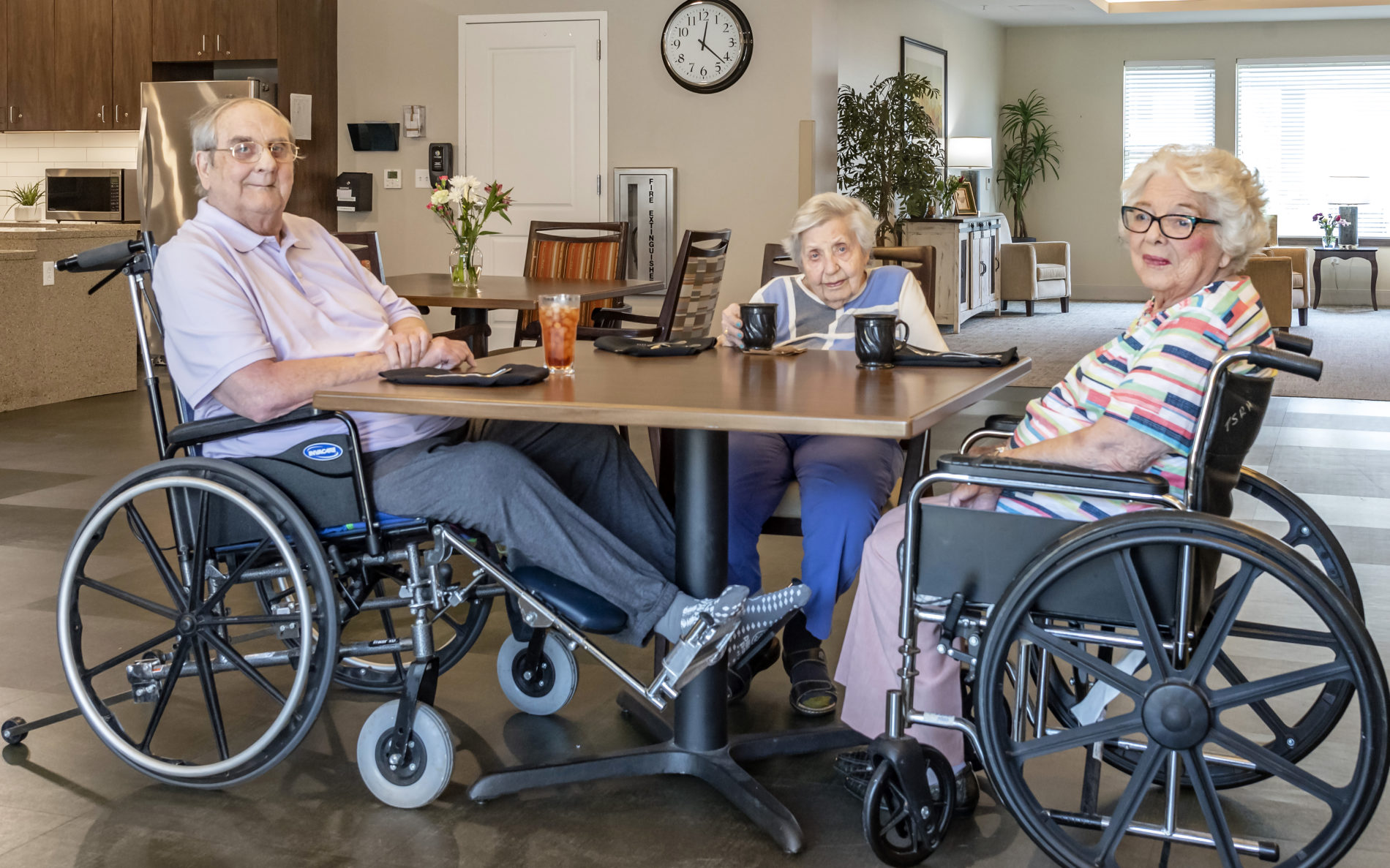 Elderly women and man in wheelchairs around table