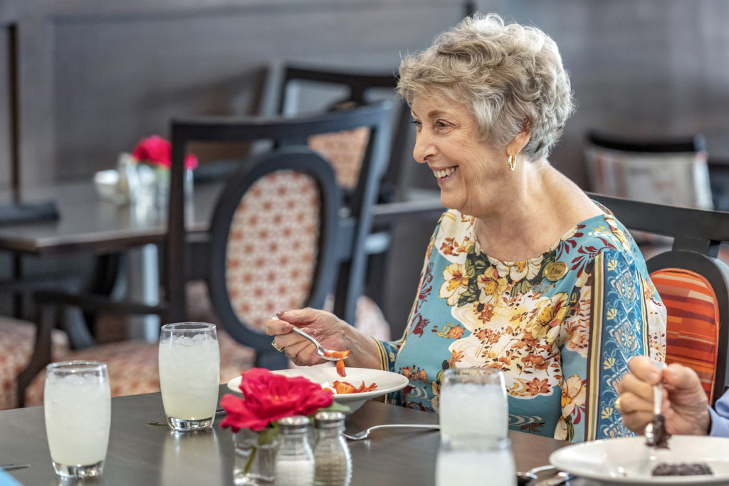 Senior woman smiling while eating at dining table