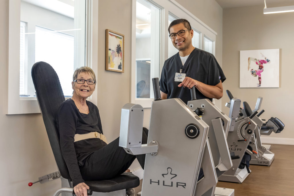 Woman smiling while on therapy machine with smiling employee helping