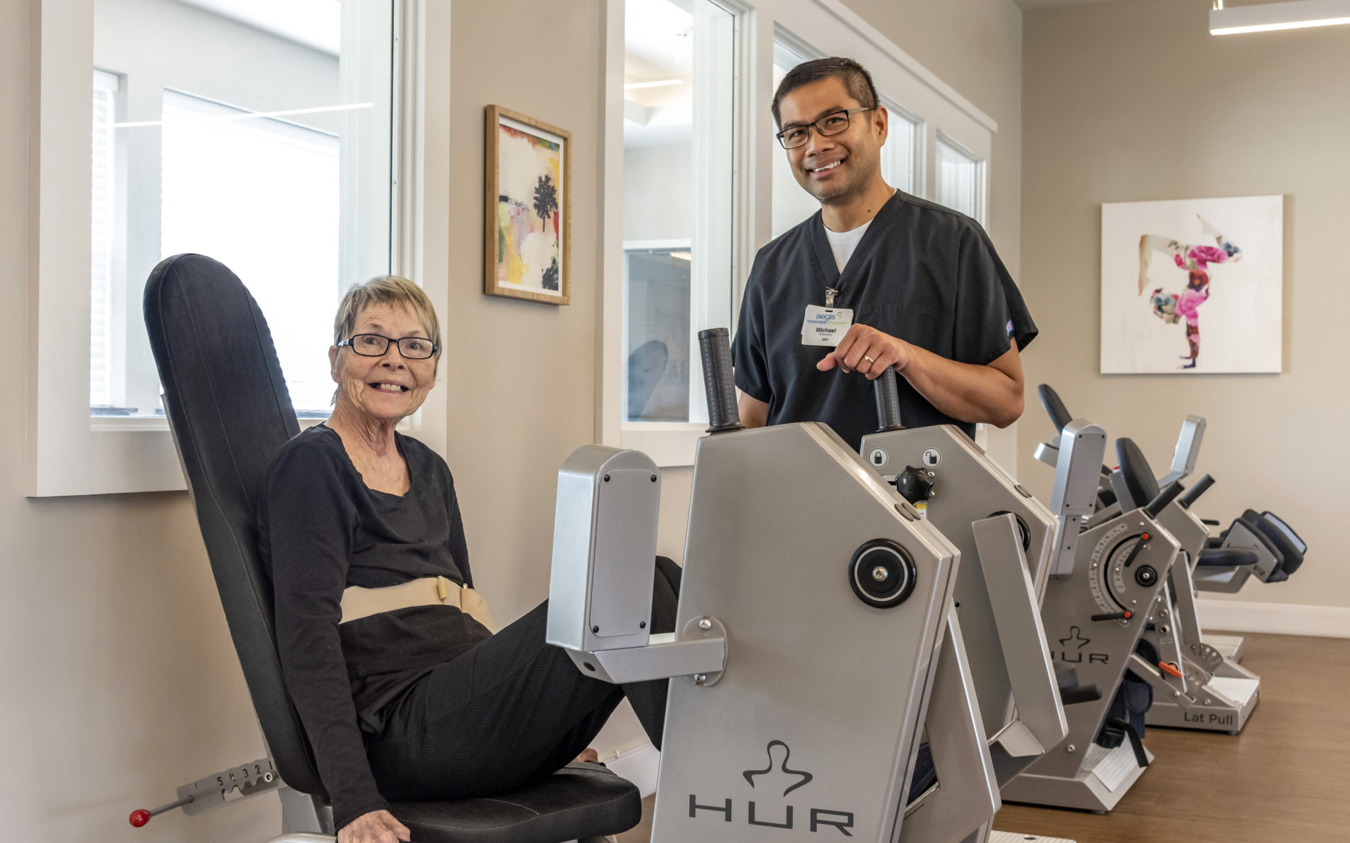 Woman smiling while on therapy machine with smiling employee helping